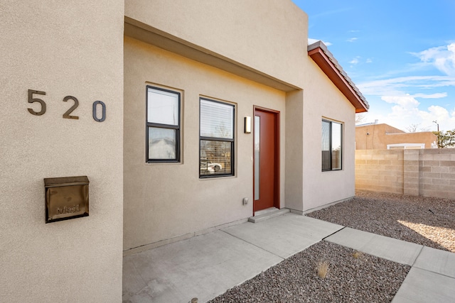 view of exterior entry featuring fence and stucco siding