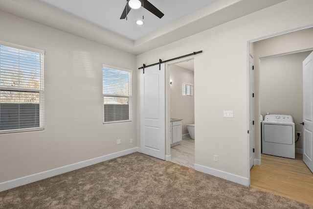 unfurnished bedroom featuring light carpet, a barn door, baseboards, connected bathroom, and washer / clothes dryer