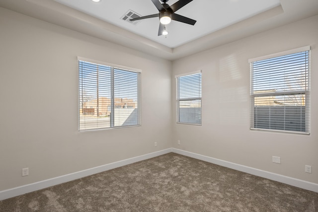 spare room with dark colored carpet, a raised ceiling, visible vents, a ceiling fan, and baseboards