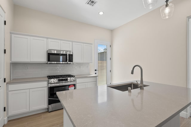 kitchen featuring tasteful backsplash, visible vents, appliances with stainless steel finishes, a kitchen island with sink, and a sink