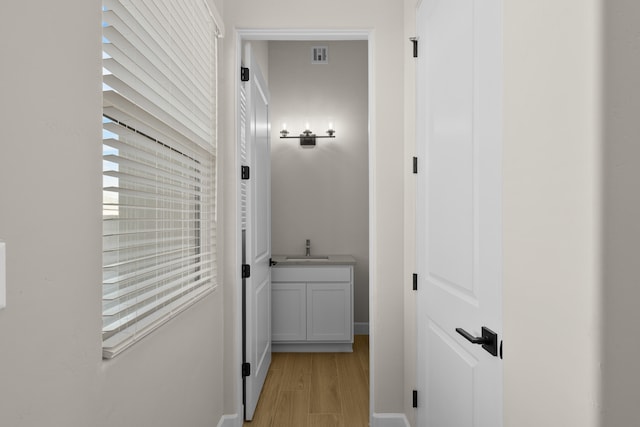 hall with a healthy amount of sunlight, light wood-style flooring, visible vents, and a sink