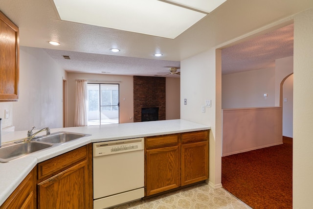 kitchen with brown cabinets, a peninsula, white dishwasher, a textured ceiling, and a sink