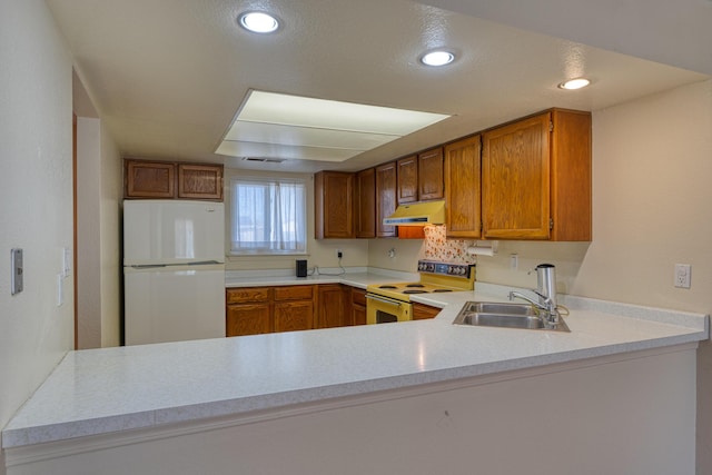 kitchen with a peninsula, white appliances, a sink, and under cabinet range hood