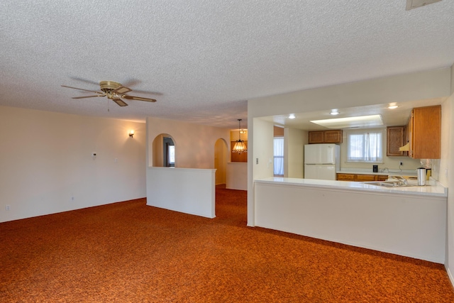 unfurnished living room with arched walkways, a textured ceiling, a sink, carpet flooring, and a ceiling fan