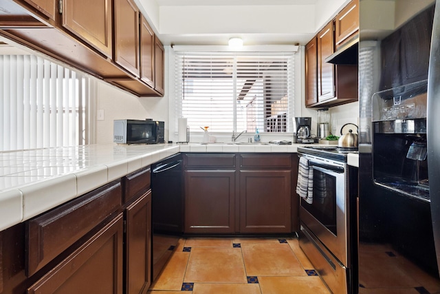 kitchen featuring light tile patterned floors, tile counters, a sink, under cabinet range hood, and black appliances