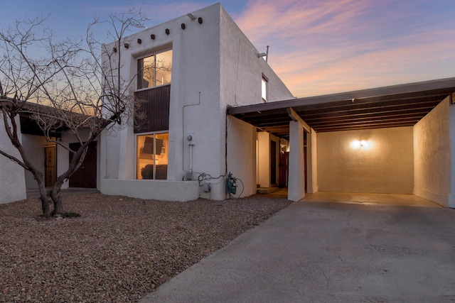 view of front facade featuring driveway, a carport, and stucco siding