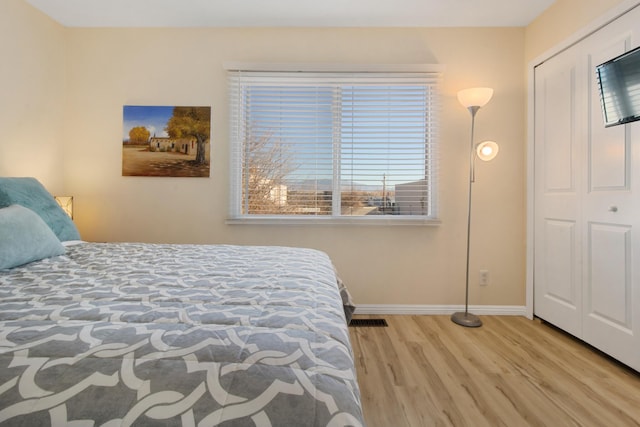 bedroom with a closet, visible vents, baseboards, and wood finished floors