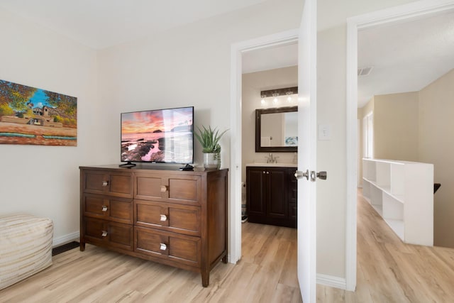 interior space with a sink, visible vents, baseboards, light wood-type flooring, and ensuite bath