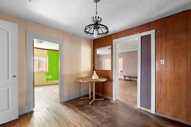 hallway featuring a textured ceiling, hardwood / wood-style floors, baseboards, and wooden walls