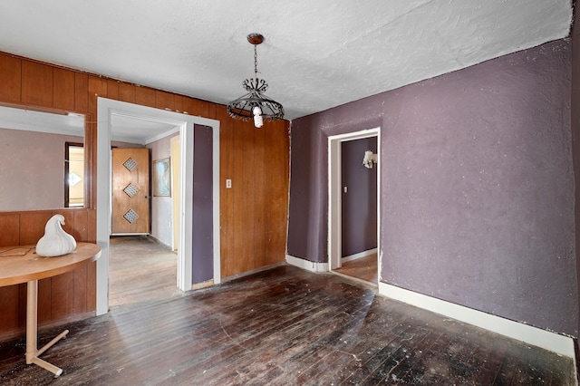 spare room with baseboards, a textured wall, hardwood / wood-style flooring, a textured ceiling, and wood walls