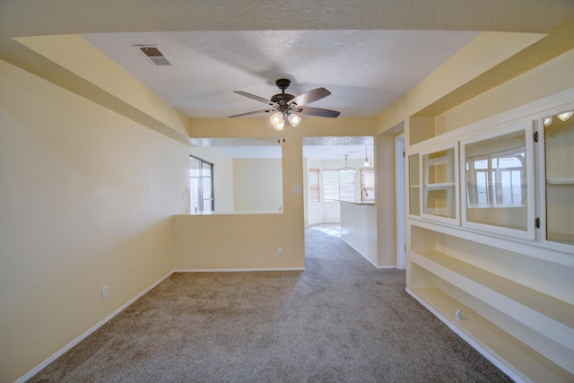 carpeted empty room with a textured ceiling, baseboards, visible vents, and a ceiling fan