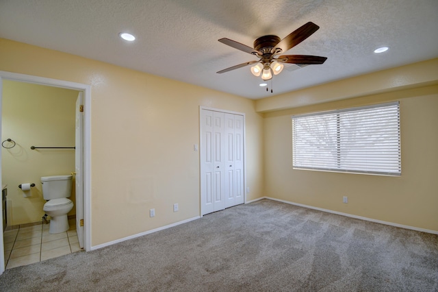 unfurnished bedroom with a textured ceiling, carpet, tile patterned floors, and ensuite bathroom