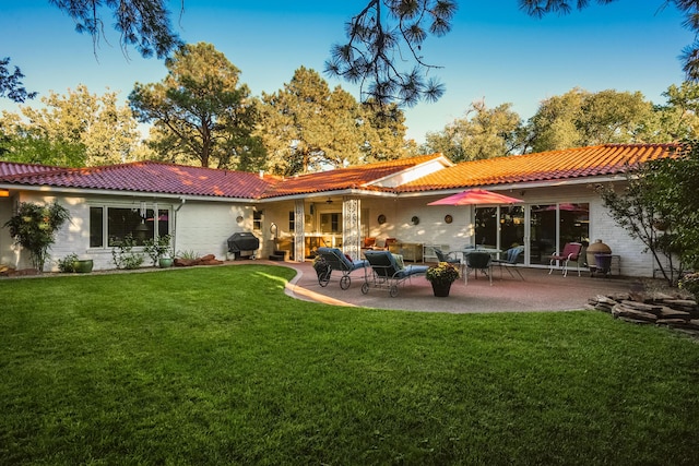 rear view of house featuring a patio, a lawn, and a tiled roof