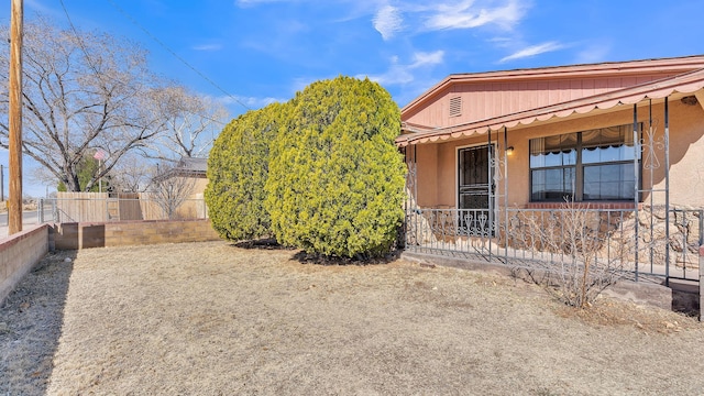 view of side of property with covered porch, fence, and stucco siding