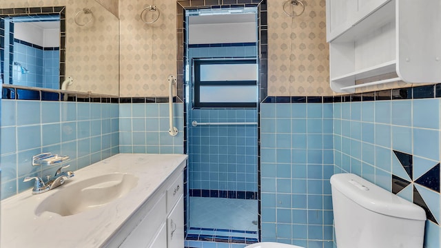 full bath featuring toilet, wallpapered walls, a tile shower, and wainscoting