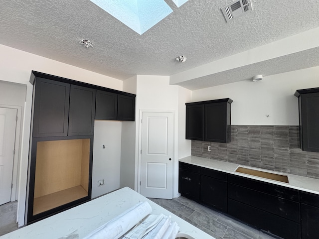 kitchen with decorative backsplash, a skylight, visible vents, and dark cabinetry