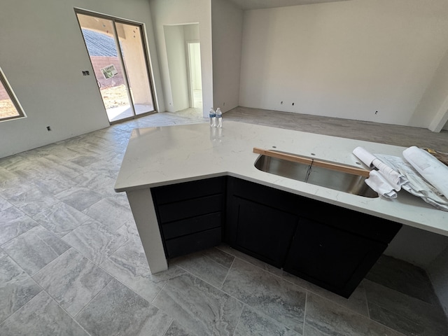 kitchen with dark cabinets, a sink, and light stone countertops