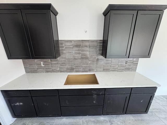 kitchen with tasteful backsplash, dark cabinetry, and light stone counters