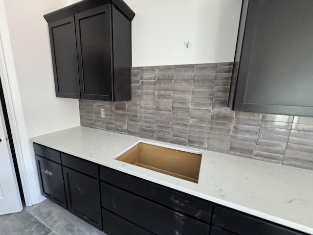 kitchen featuring tasteful backsplash, dark cabinetry, a sink, and light stone countertops