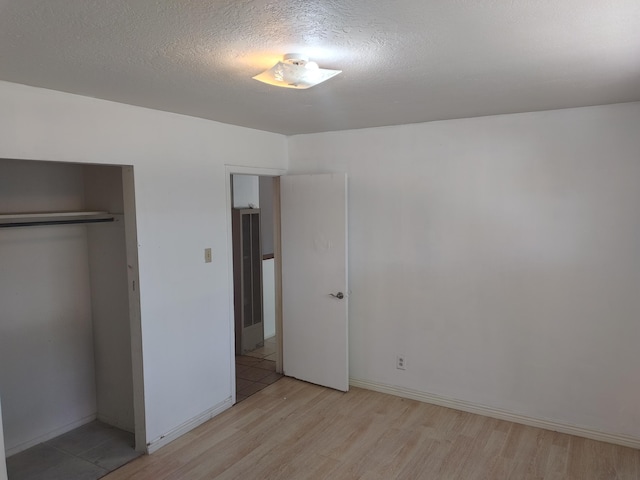 unfurnished bedroom featuring a closet, baseboards, light wood-style floors, and a textured ceiling