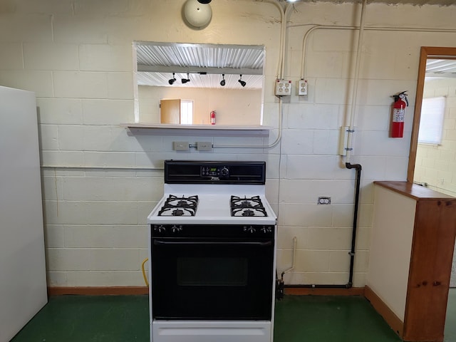 kitchen with gas range, concrete block wall, and freestanding refrigerator