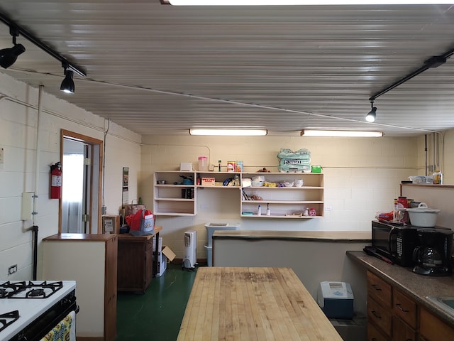 kitchen with gas stove, concrete block wall, black microwave, and open shelves