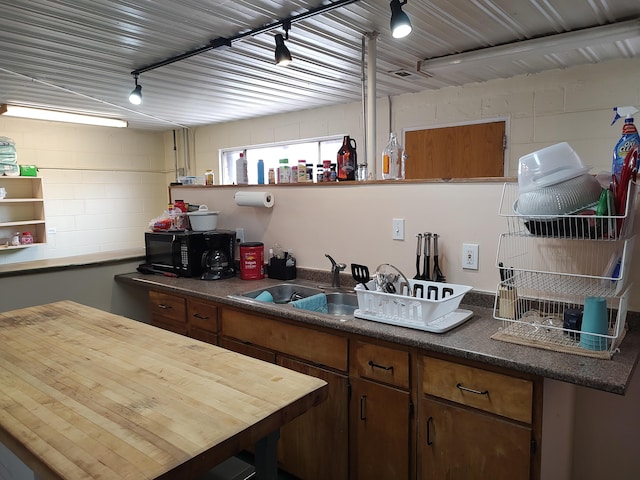 kitchen featuring concrete block wall, open shelves, a sink, rail lighting, and black microwave