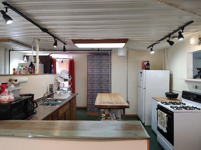 kitchen featuring concrete block wall, freestanding refrigerator, a sink, gas range oven, and black microwave