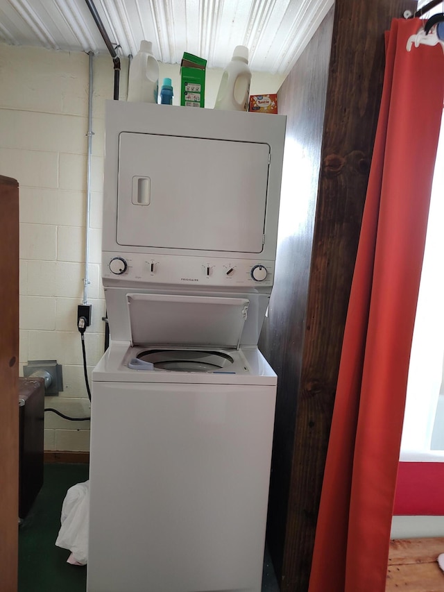 washroom with concrete block wall, laundry area, and stacked washing maching and dryer