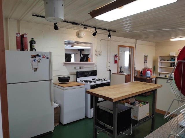 kitchen with gas range, concrete block wall, butcher block counters, and freestanding refrigerator