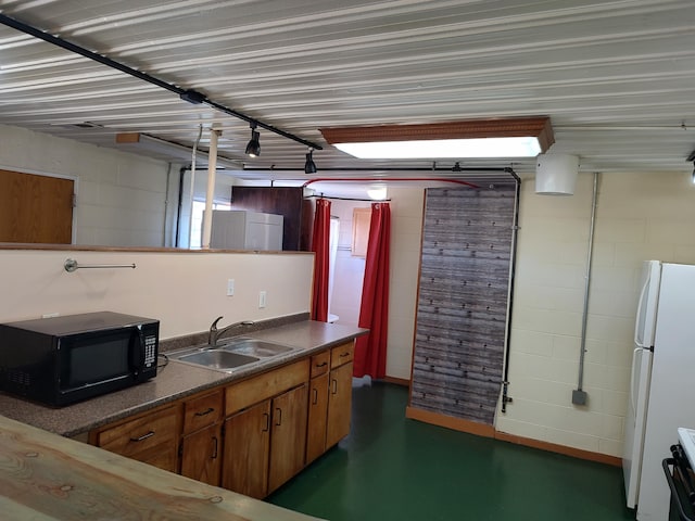 kitchen featuring dark countertops, black microwave, concrete flooring, freestanding refrigerator, and a sink