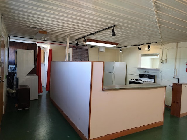 kitchen with rail lighting, concrete block wall, white appliances, and concrete floors