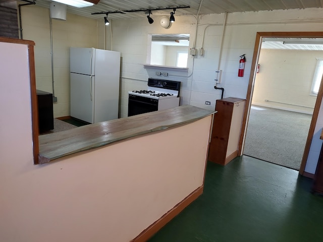 kitchen with white appliances, concrete block wall, finished concrete flooring, a peninsula, and track lighting