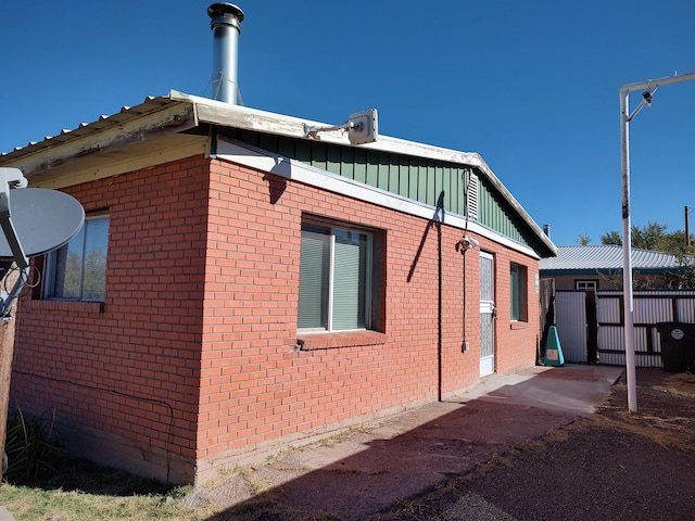 view of property exterior with brick siding, board and batten siding, and fence