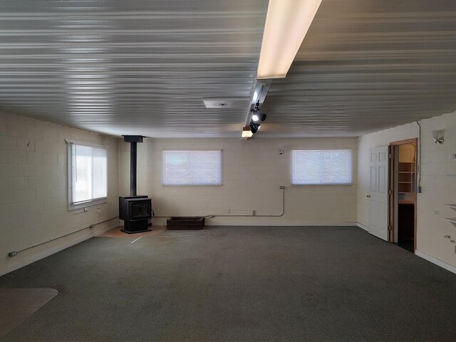 interior space with dark carpet, concrete block wall, and a wood stove