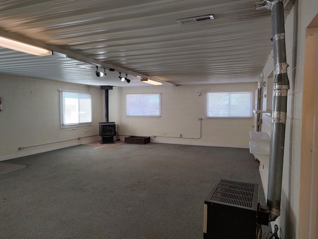 basement featuring carpet flooring, a wood stove, concrete block wall, and visible vents