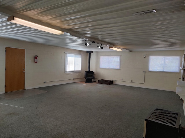 unfurnished living room featuring visible vents, concrete block wall, and a wood stove