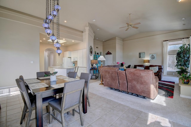 dining space featuring arched walkways, light tile patterned floors, light carpet, ceiling fan, and vaulted ceiling