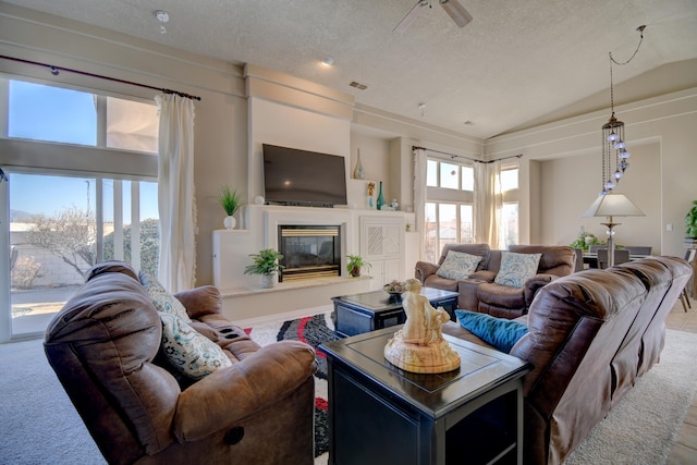 living area featuring carpet floors, lofted ceiling, visible vents, a glass covered fireplace, and a textured ceiling