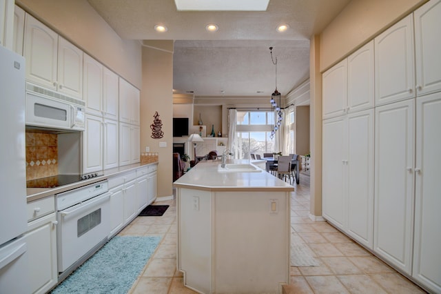 kitchen with recessed lighting, a kitchen island with sink, a sink, white cabinetry, and white appliances