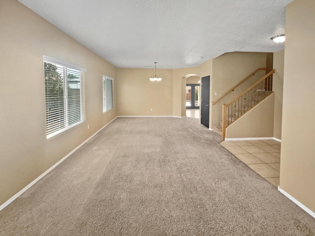 carpeted empty room with a textured ceiling, arched walkways, stairs, tile patterned floors, and an inviting chandelier