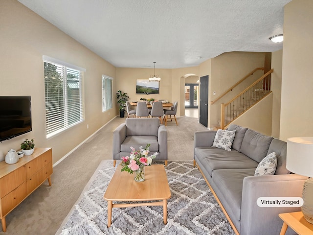 carpeted living room featuring baseboards, stairs, arched walkways, and a textured ceiling