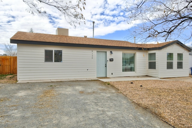 ranch-style home featuring driveway, a shingled roof, a patio, a chimney, and fence