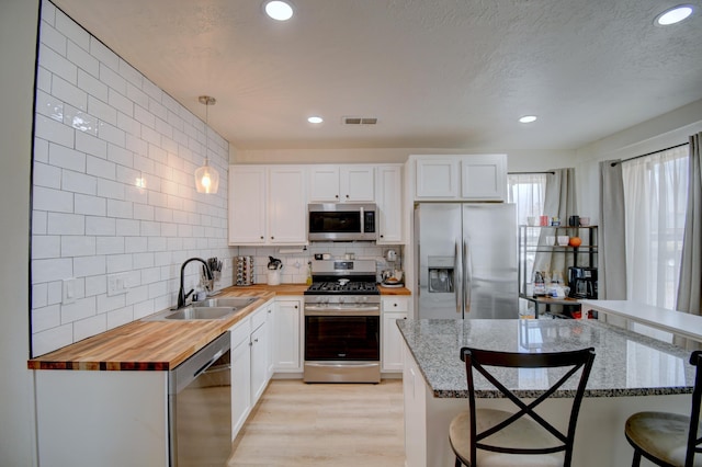 kitchen featuring stainless steel appliances, visible vents, wooden counters, a sink, and a kitchen bar