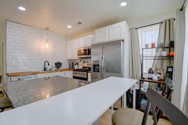 kitchen with tasteful backsplash, visible vents, appliances with stainless steel finishes, a kitchen breakfast bar, and a sink