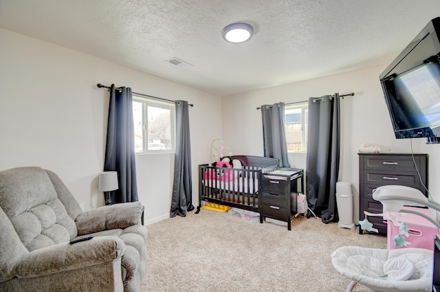 carpeted bedroom featuring a textured ceiling, multiple windows, and visible vents