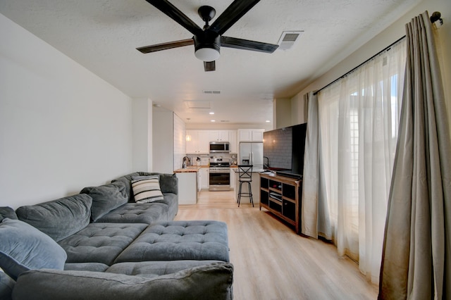 living area featuring visible vents, light wood-style flooring, and a ceiling fan