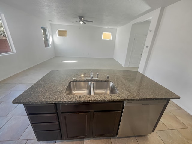 kitchen featuring dishwasher, open floor plan, dark stone countertops, a kitchen island with sink, and a sink