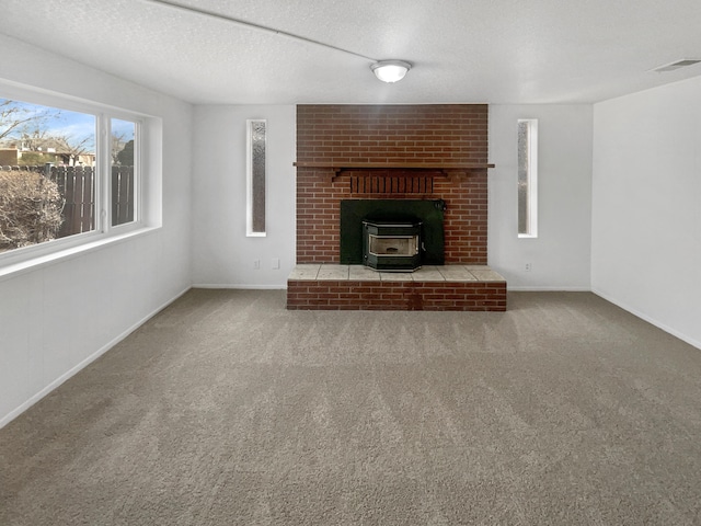 unfurnished living room with a textured ceiling, carpet floors, visible vents, baseboards, and a wood stove