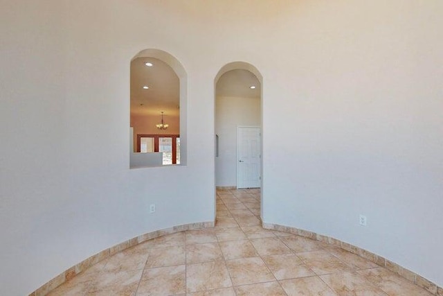 empty room with arched walkways, light tile patterned floors, an inviting chandelier, and baseboards